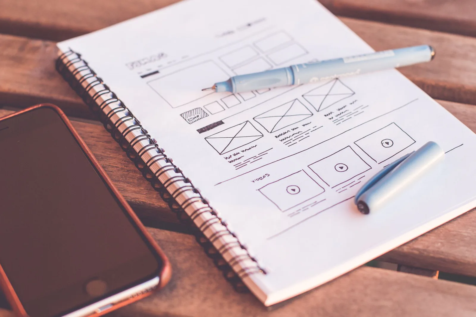 Hand-drawn wireframe sketches in a notebook beside a smartphone